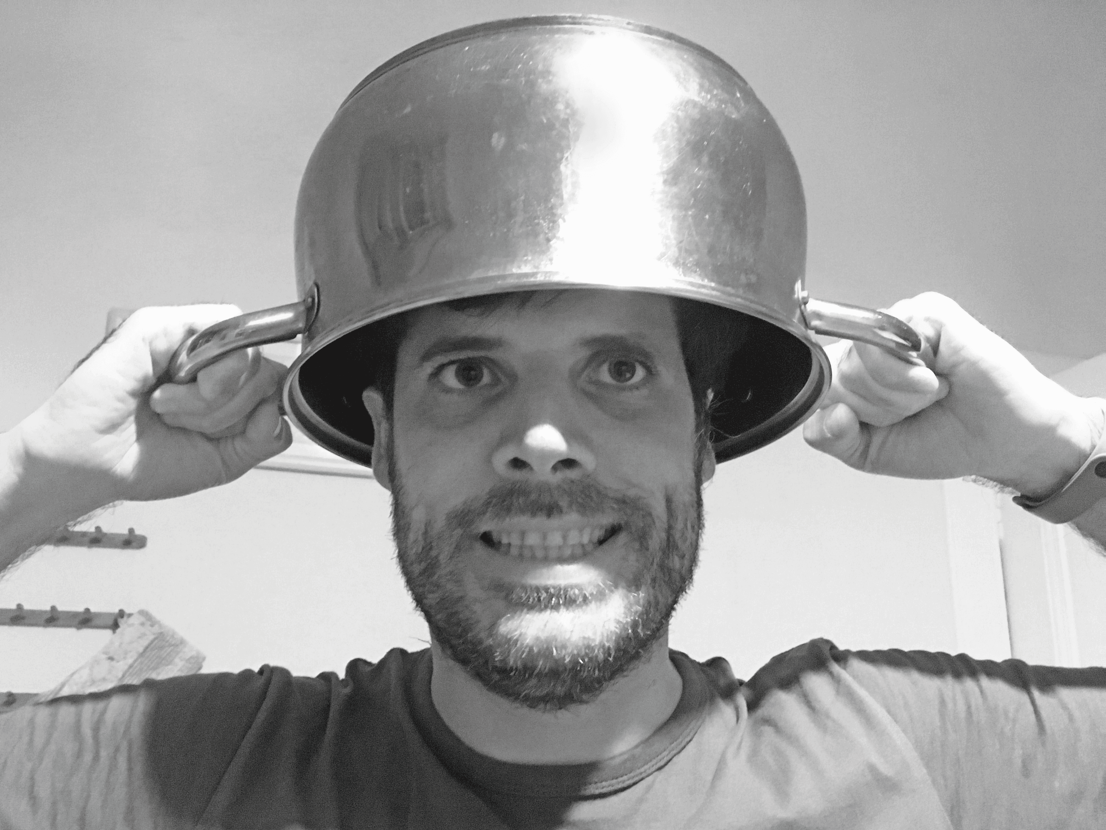 Primer plano de Eric Romero. Es una foto en blanco y negro. Eric sonríe a cámara, luciendo una olla en la cabeza cual distinguido sombrero.