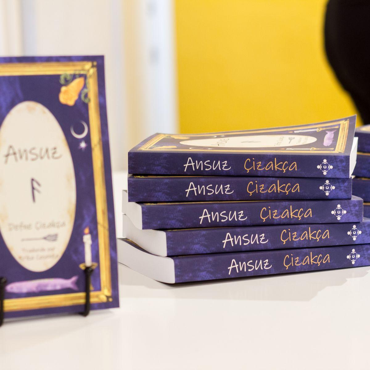 Foto tomada por Gigi Caffarena durante la presentación del libro Ansuz en Barcelona. Sobre una mesa hay un atril aque sostiene un ejemplar de manera tal que se vea la portada; a su lado, una pila con cinco ejemplares que muestran el lomo hacia la cámara.
