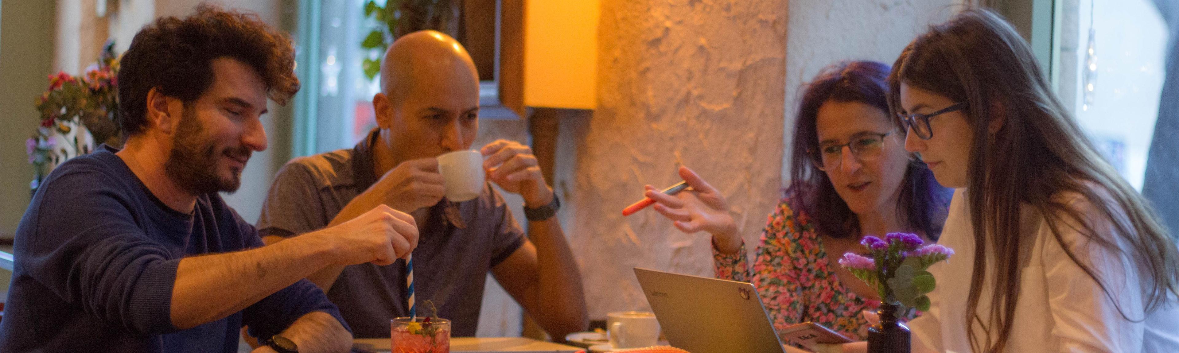 El equipo de Ciempiés (Maui Barone, Erika Cosenza, Javier Rey y Wenceslao Zuloaga) sentado aldedor de una mesa de bar sobre la que se pueden apreciar libros, ordenadores, papeles y bolígrafros. 