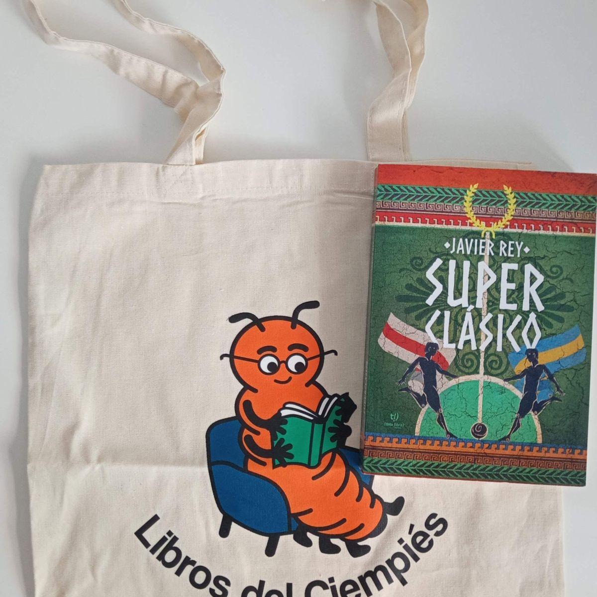 Una foto de una tote bag de Ciempiés y un ejemplar del libro «Superclásico», primera novela escrita por Javier Rey.