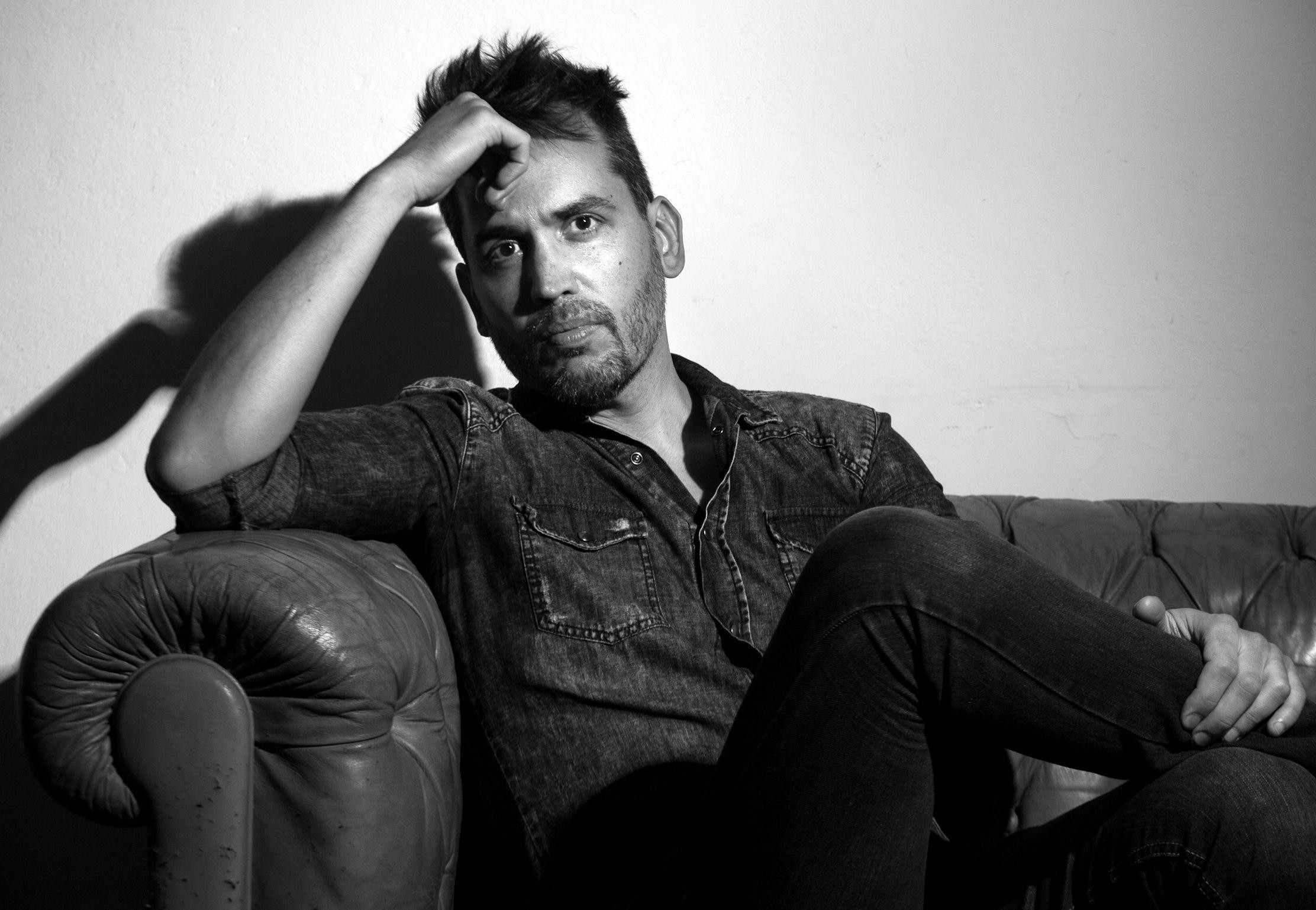 Foto en blanco y negro de Maximiliano Poter. Está sentado en un sillón, acodado sobre el apoyabrazos y apoya la cabeza sobre la mano derecha. Mira directamente a cámara con expresión seria.